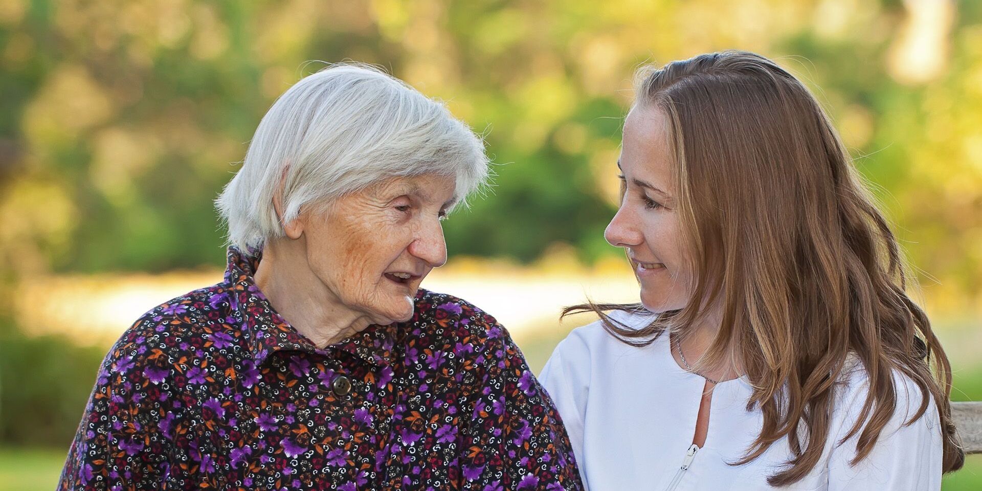 Eine Pflegerin und eine ältere Dame sitzen draußen auf einer Bank